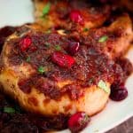A closeup view of a pork chop, in a pomegranate sauce with dotted cranberries around it too.
