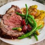 A plate with prime rib, potatoes and green bean salad.