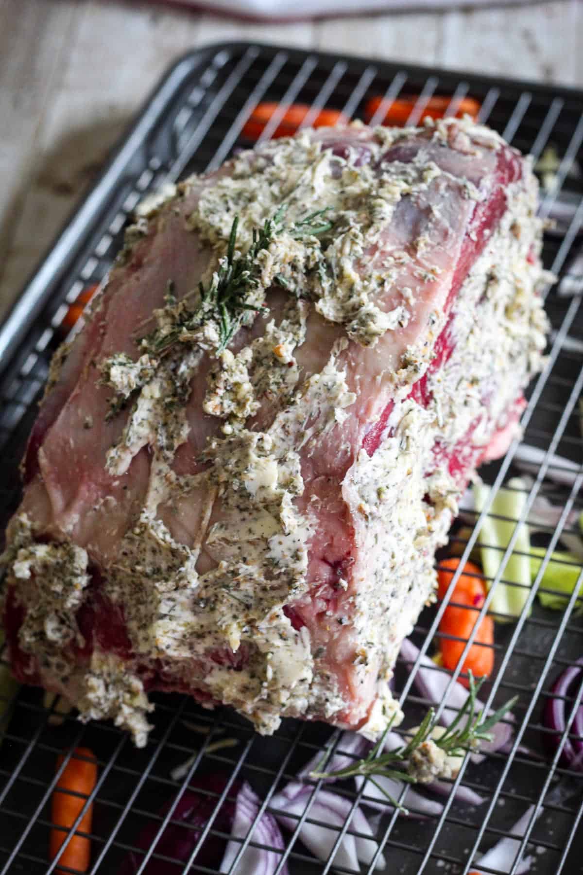 Applying herbed butter all over the prime rib then adding the meat over a rack. 