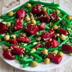 A round platter with a green beans salads dotted with red beets and pistachios.
