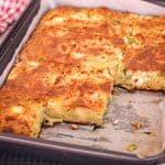 A leeks and cornmeal casserole or savory pie, shown in the baking tray, sliced already. Some slices have already been served so there are missing spots in the tray.