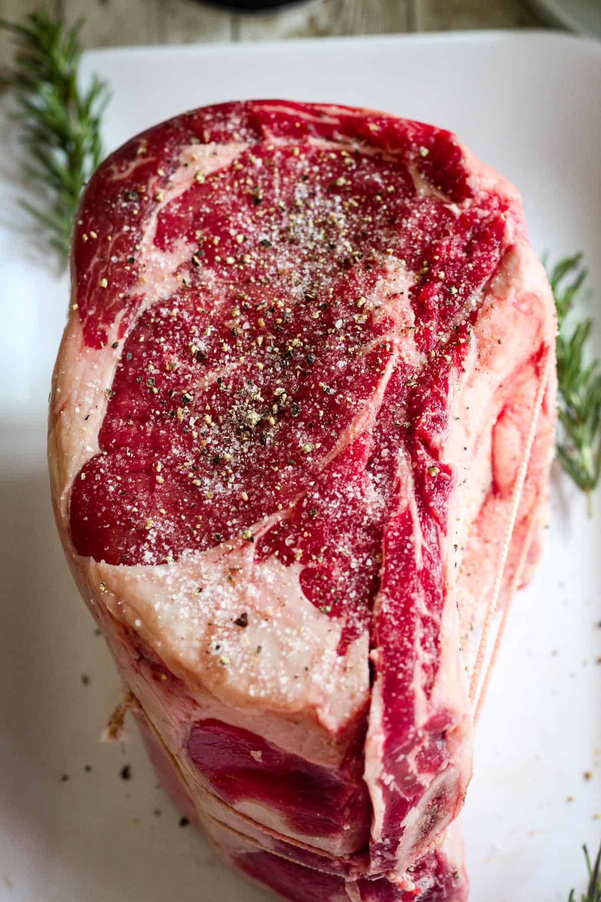 Seasoned prime rib cut, raw shown on a platter. 