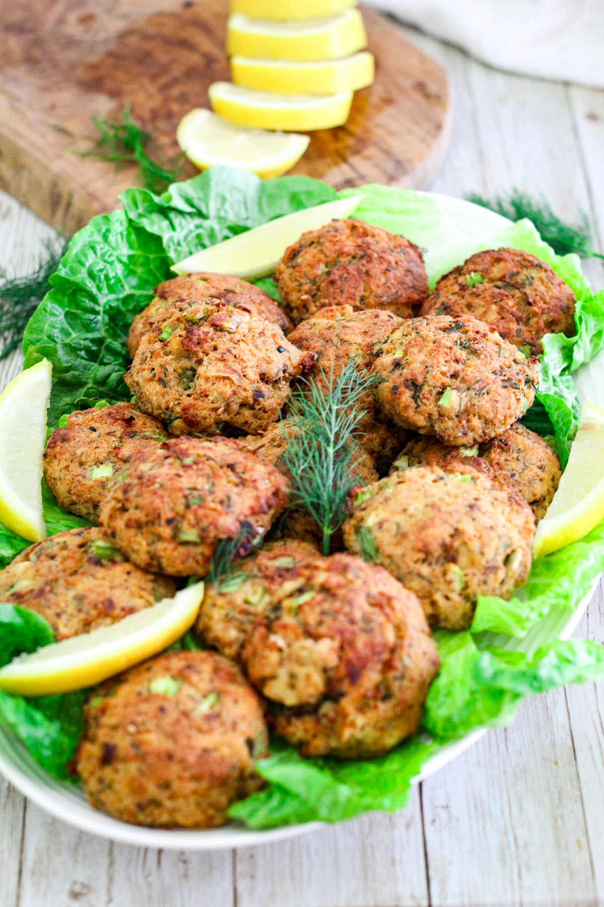 Salmon patties or salmon cakes on a serving platter, shown over lettuce and garnished with lemon slices.