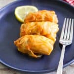 A plate with three cabbage rolls garnished with a lemon slice.