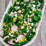 A platter with a greens and asparagus salad, showing also radishes, feta and other ingredients.