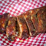 A rack of BBQ ribs shown on a checkered red/white parchment paper.