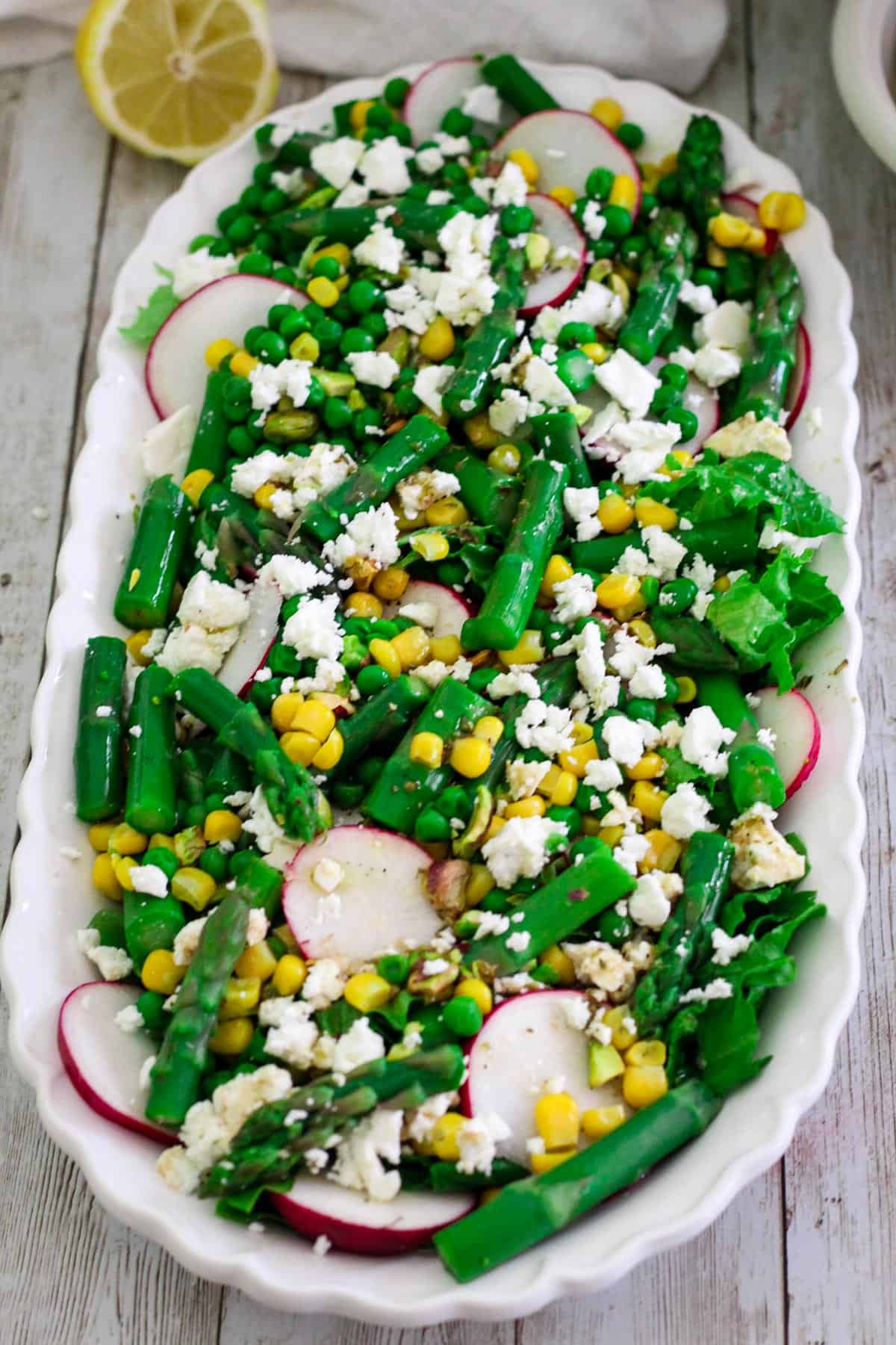 A platter with a greens salad whre you can see asparagus, radishes, corn, green peas, feta cheese and more.
