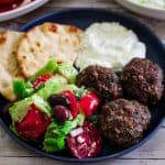 A plate with meatballs, salad and yogurt dip with pita bread.