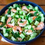 A blue salad bowl showing a cucumber shrimp salad, Shrimp, cucumbers, green peas and cilantro are visible on the bowl.