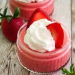 Strawberry mousse served in glass shallow cups, topped with whipped cream and slices of fresh strawberry.