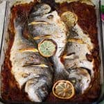 A dish with baked whole fish, sea bream over onions and tomatoes sauce, just baked.