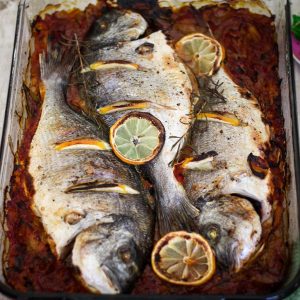 A dish with baked whole fish, sea bream over onions and tomatoes sauce, just baked.