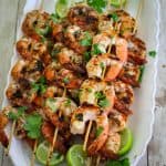 Grilled shrimp skewers in a platter garnished with lime and cilantro.