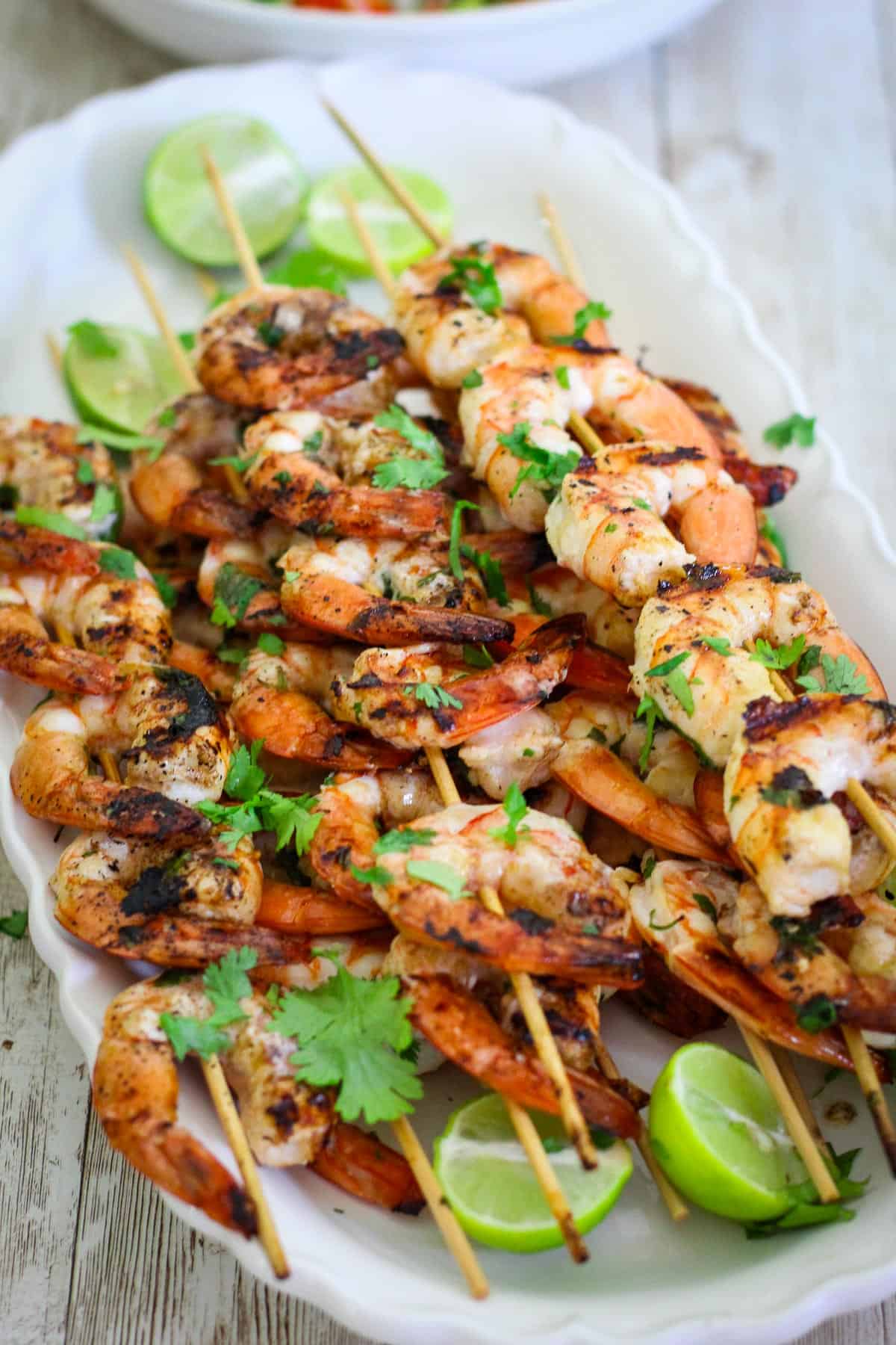 Shrimp skewers on a platter, garnished with cilantro and lime. 