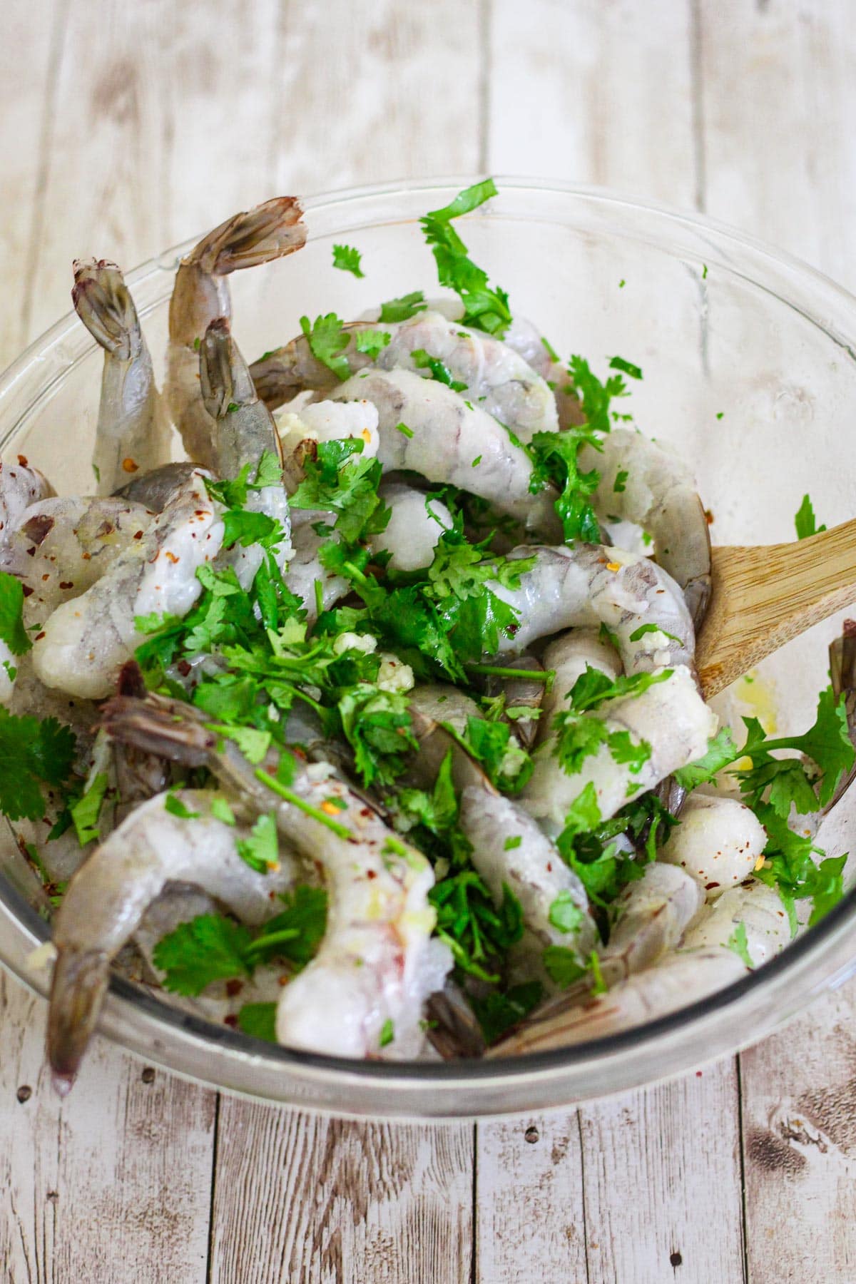 Uncooked shrimp with cilantro and other seasonings in a glass bowl, ready to marinate. 