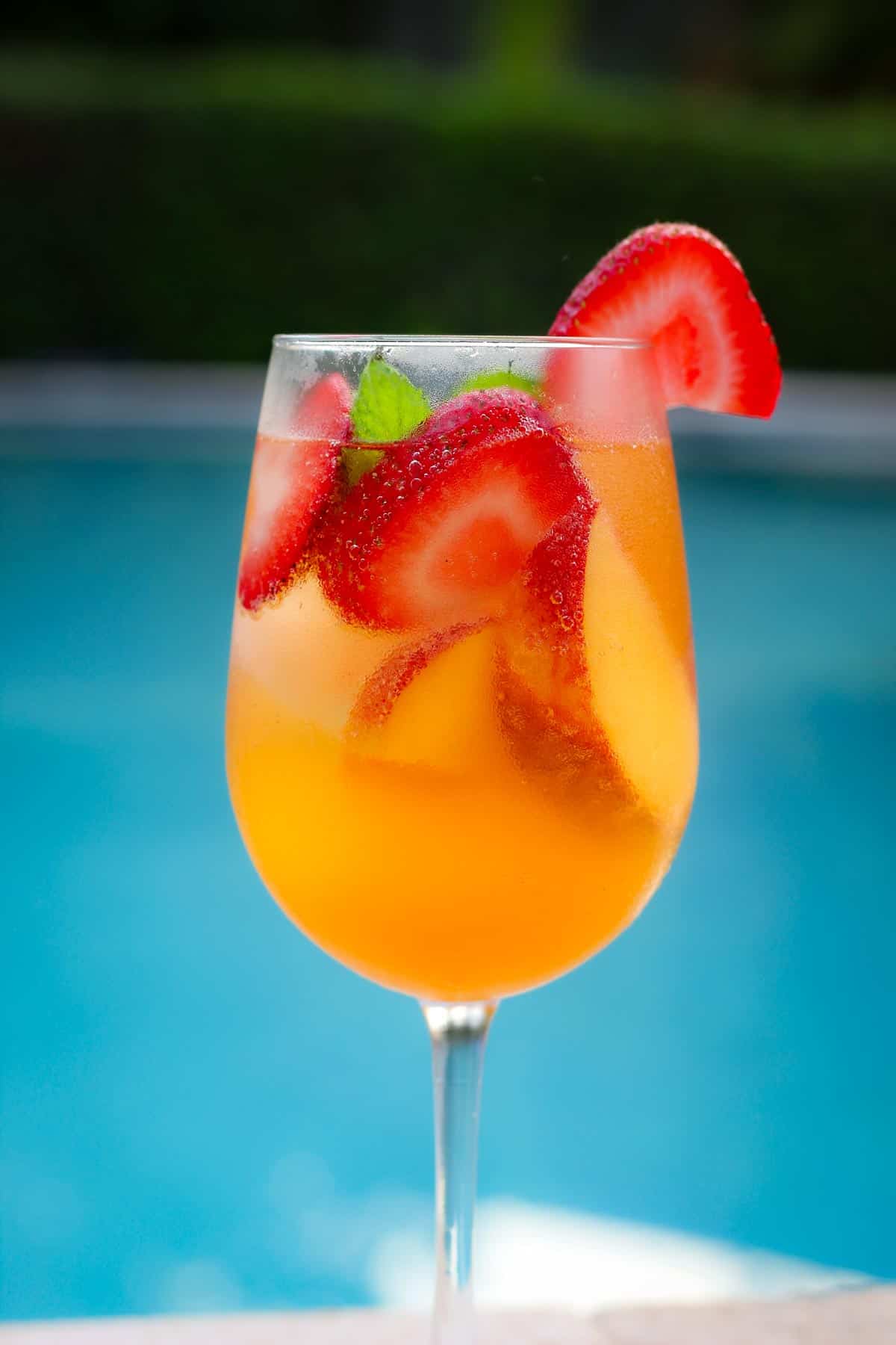 A rose sangria on a wine glass with slices of strawberries and peaches. 