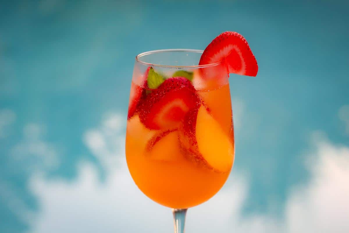 A wine glass showing a rose sangria with peaches and strawberries next to a pool.