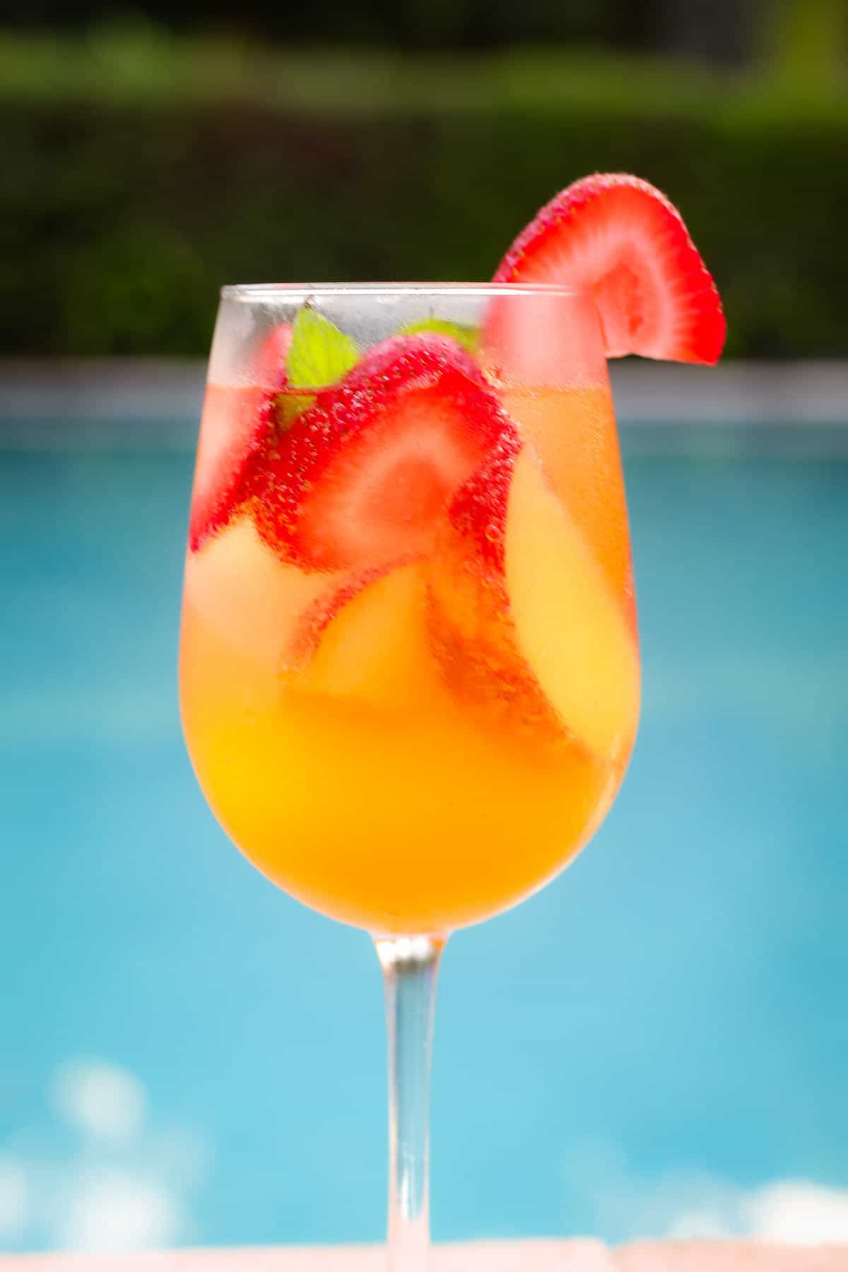 A wine glass with peaches, strawberries and rose sangria next to the pool. 