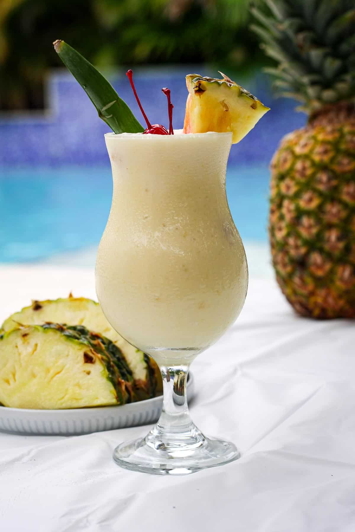 A dreamy poolside piña colada drink, garnished with maraschino cherries and a pineapple wedge. 