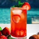 Strawberry mojito shown next to the pool. Drink is garnished with fresh strawberry slices and mint leaves.