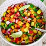 A salad bowl with chopped bell peppers of different colors, cilantro, red onion and limes.