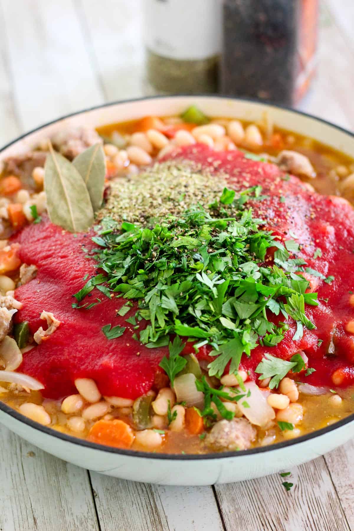 Adding tomato sauce, bay leaves, fresh parsley and other herbs and seasonings to the pot. 