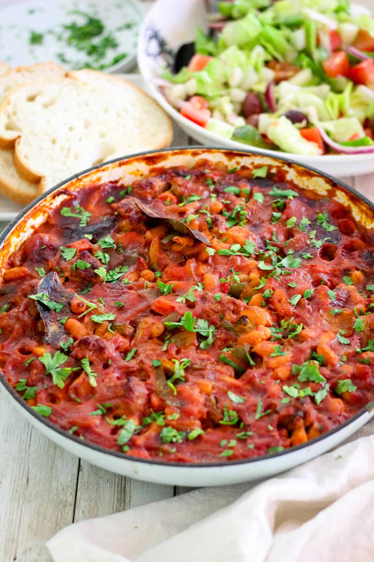 A Dutch Oven or braiser showing a baked beans dish with sausages, garnished with parsley. 
