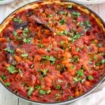 Baked beans and sausages shown on a braiser, just cooked. Dish is garnished with fresh parsley, ready to serve.
