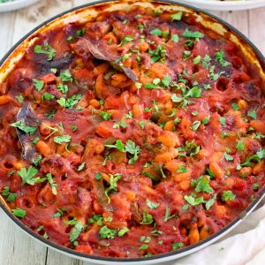 Baked beans and sausages shown on a braiser, just cooked. Dish is garnished with fresh parsley, ready to serve.