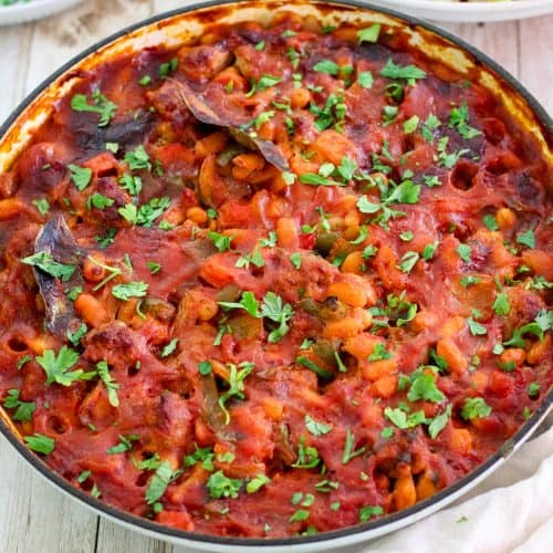 Baked beans and sausages shown on a braiser, just cooked. Dish is garnished with fresh parsley, ready to serve.