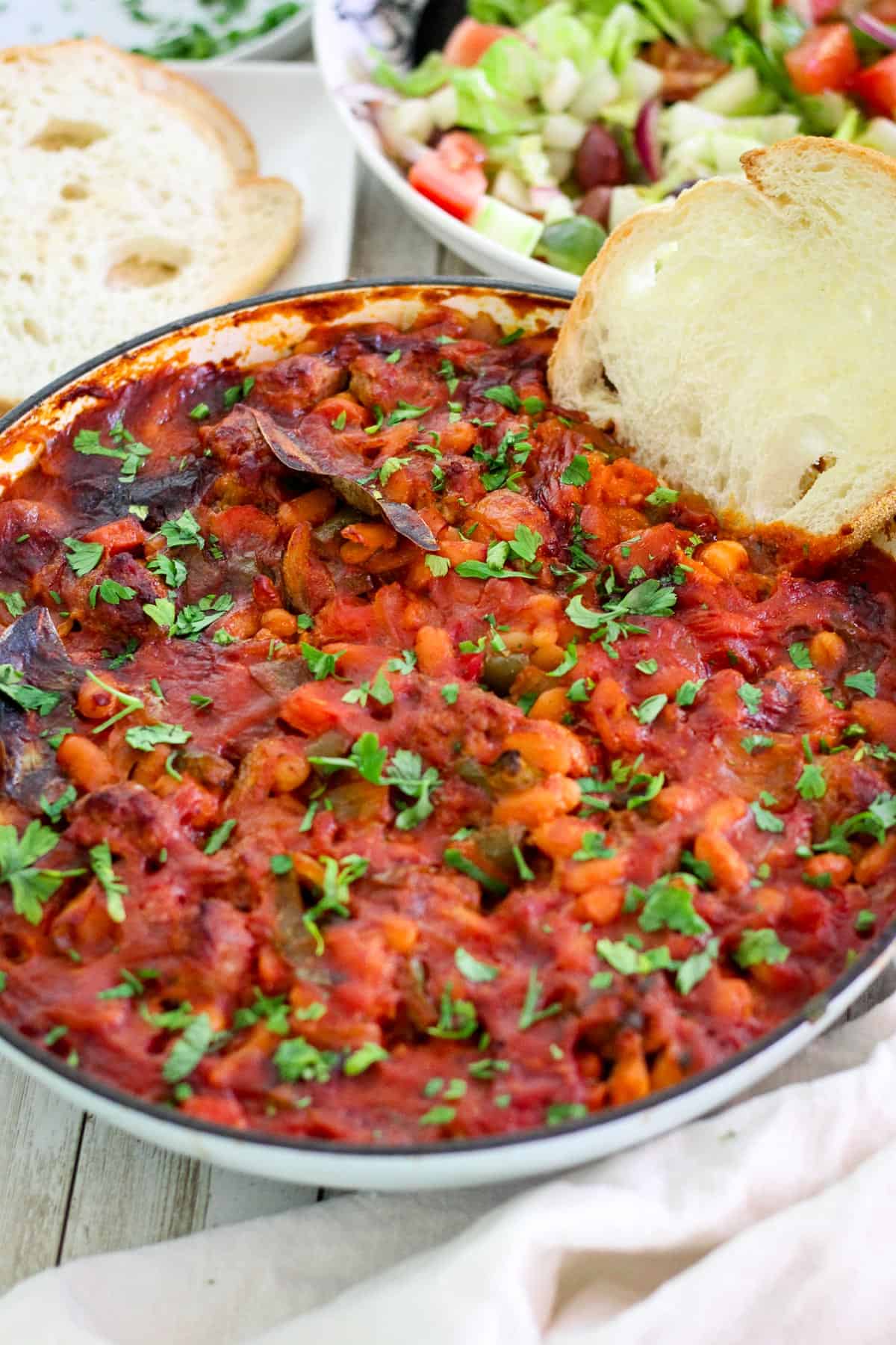 Final dish cooked, baked beans and sausage, already garnished shown with a slice of bread already dipped in, ready to serve. 