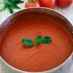 A pot with marinara sauce, garnished with fresh basil.