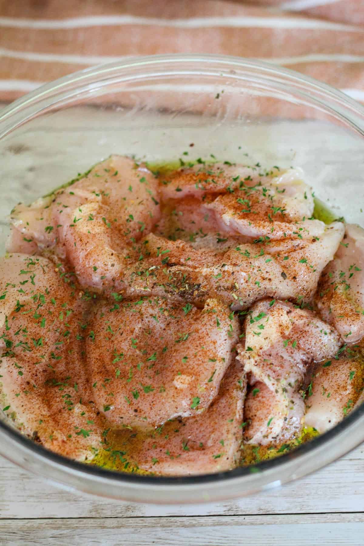 Chicken breasts in a bowl marinating with spices. 