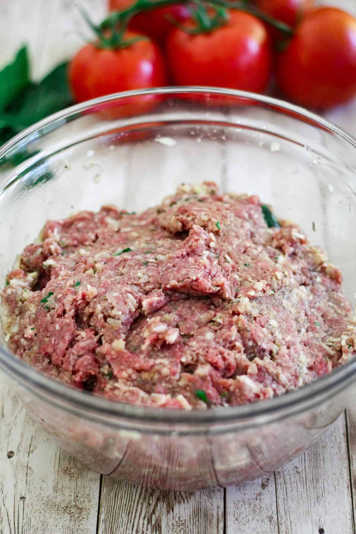 All the ingredients for meatballs are mixed into a dough like consistency in a glass bowl. 