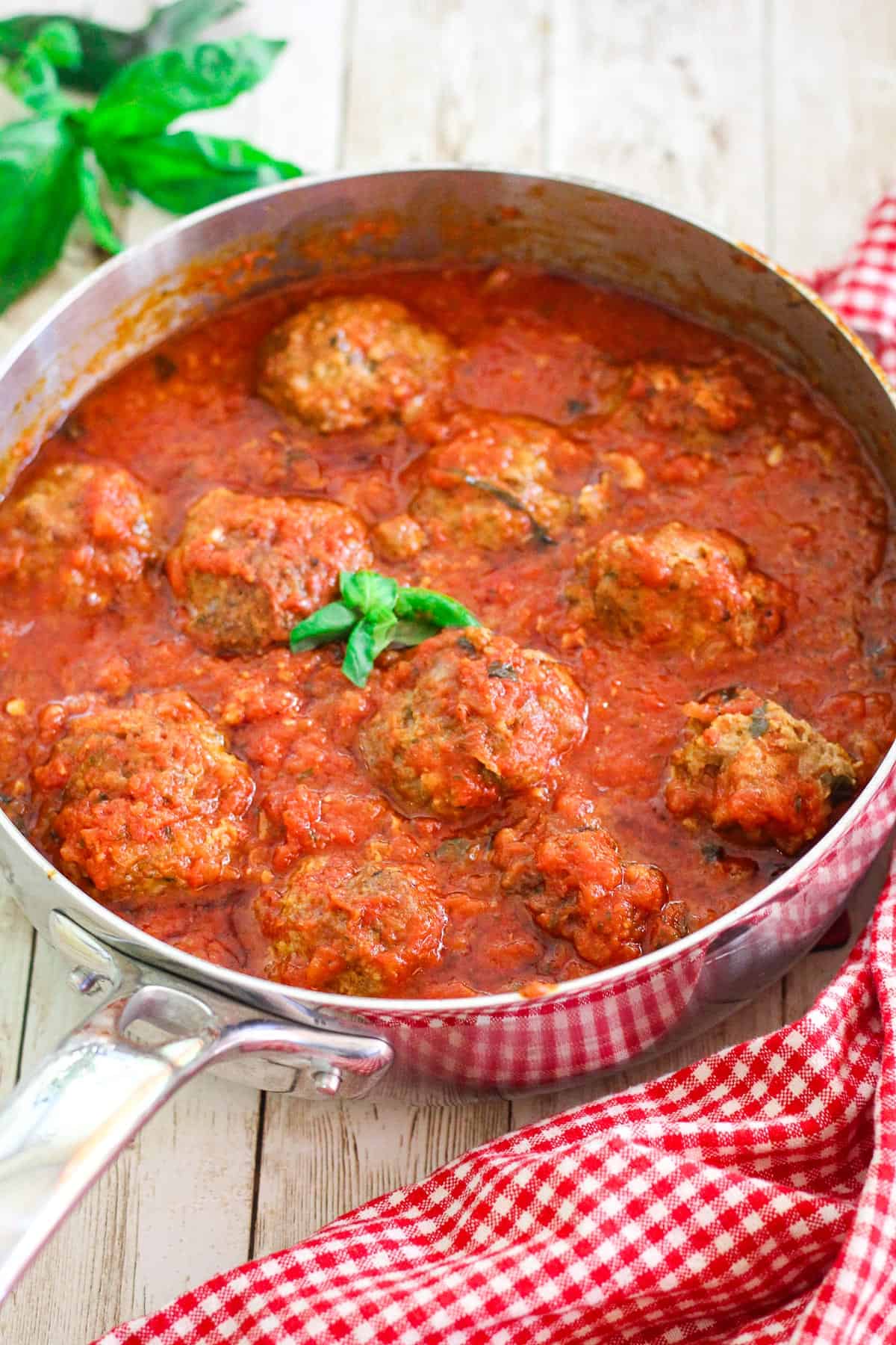 Meatballs simmered in marinara sauce, shown in a deep skillet, garnished with basil.