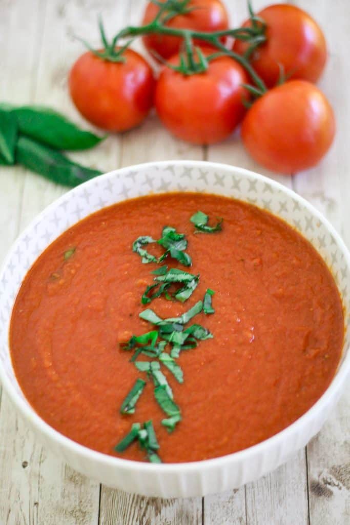 A white bowl with homemade marinara sauce, garnished with chopped basil leaves.
