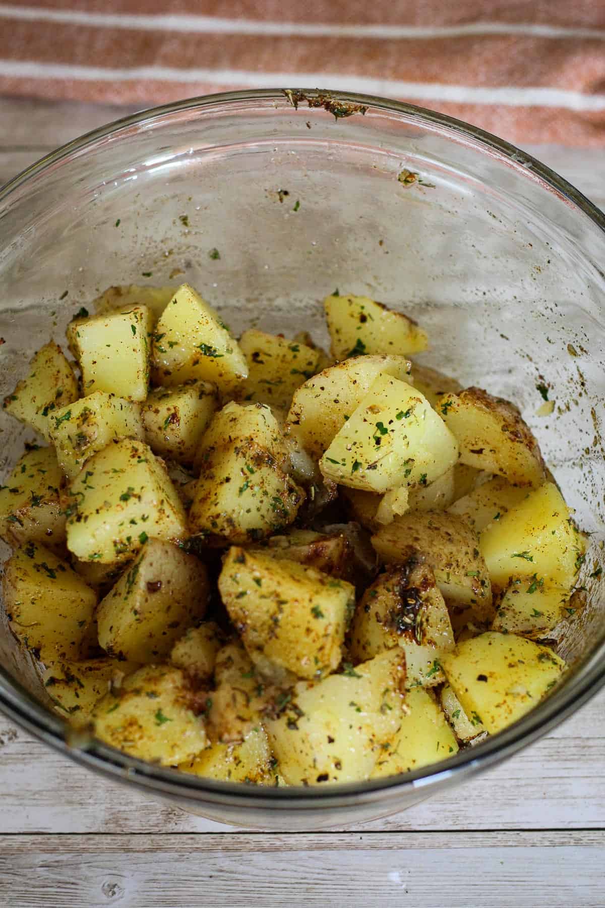 A glass bowl with seasoned potatoes.