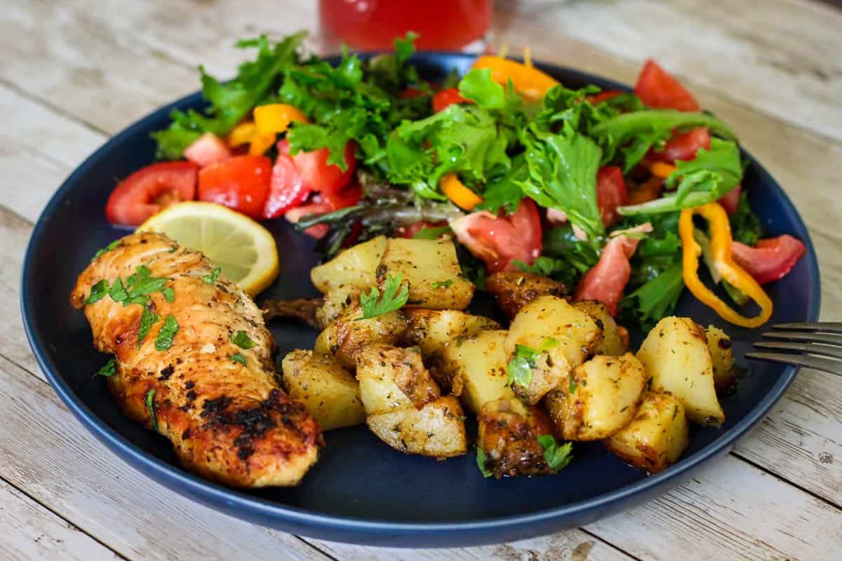 A dinner plate showing a piece of cooked chicken breast, potatoes and a salad.
