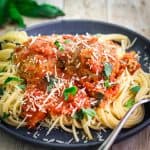 A blue plate with spaghetti, topped with meatballs and red sauce.