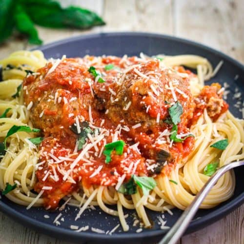 A blue plate with spaghetti, topped with meatballs and red sauce.