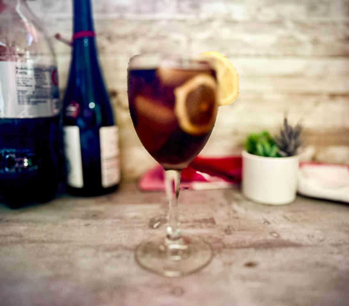 A wine glass with kalimotxo cocktail - wine and coca cola mixed over ice and garnished with lemon slices. 