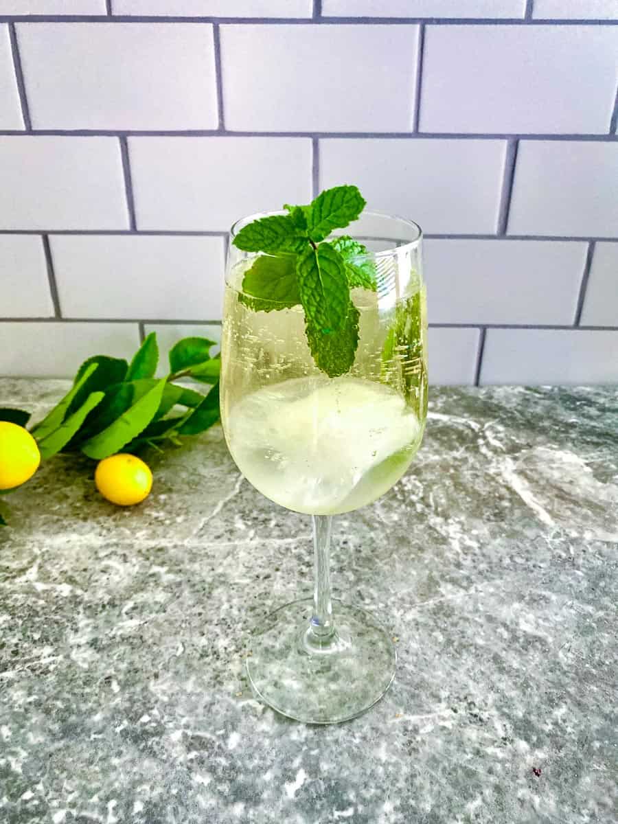 A wine glass with limoncello spritz, garnished with mint leaves. 