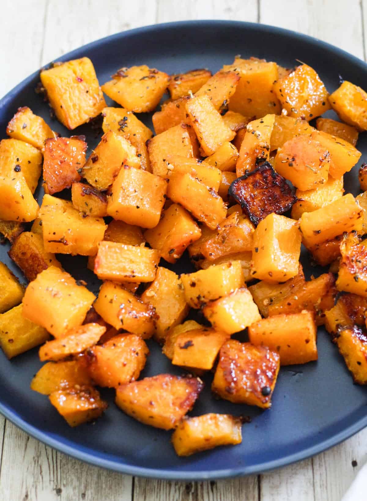 Plated, roasted butternut squash in bite size cubes. The squash looks caramelized and seasoned.