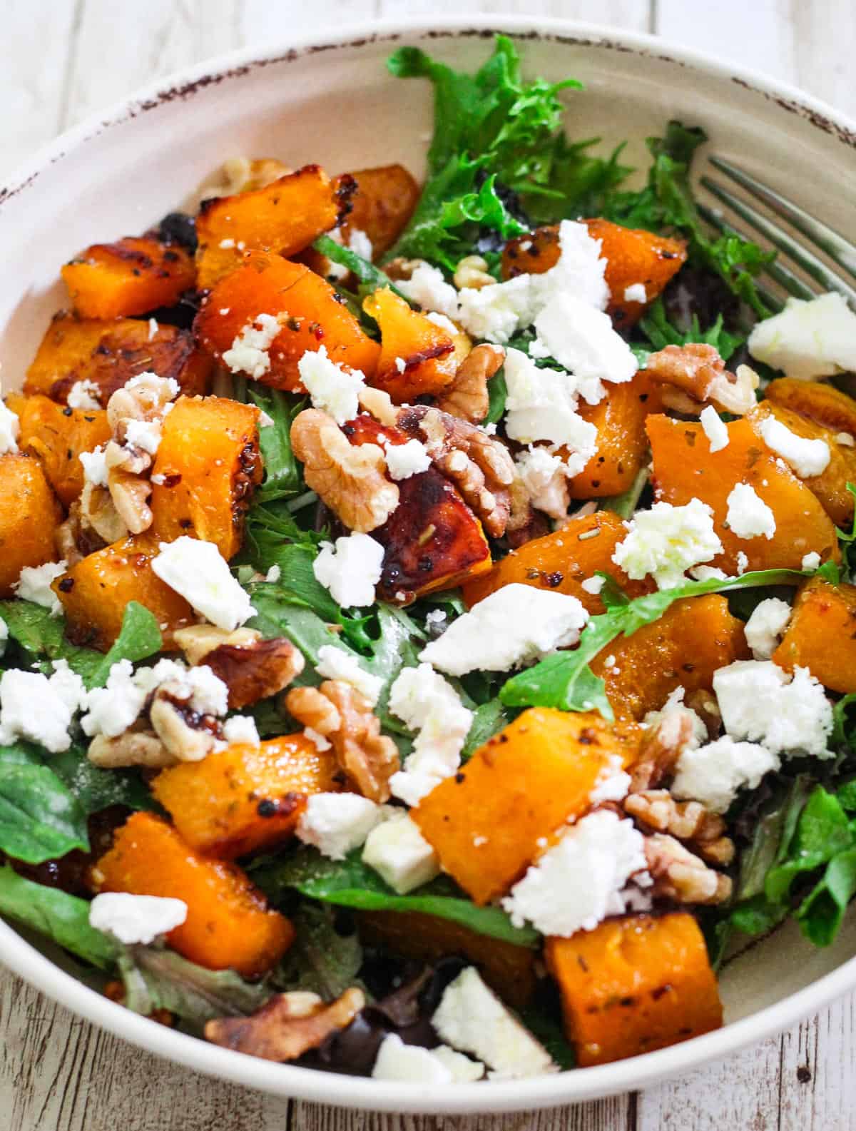 Roasted butternut squash on a salad with greens, feta cheese and walnuts. 