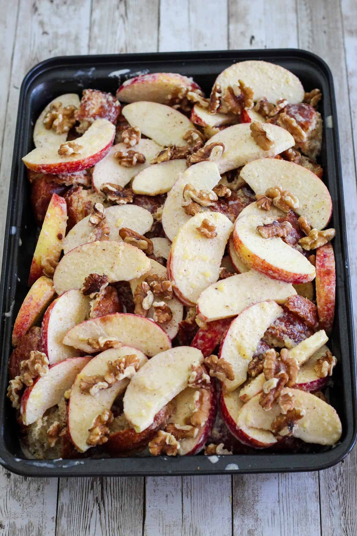 Breakfast casserole with croissants, apples and walnuts before baking, ready on a casserole dish.