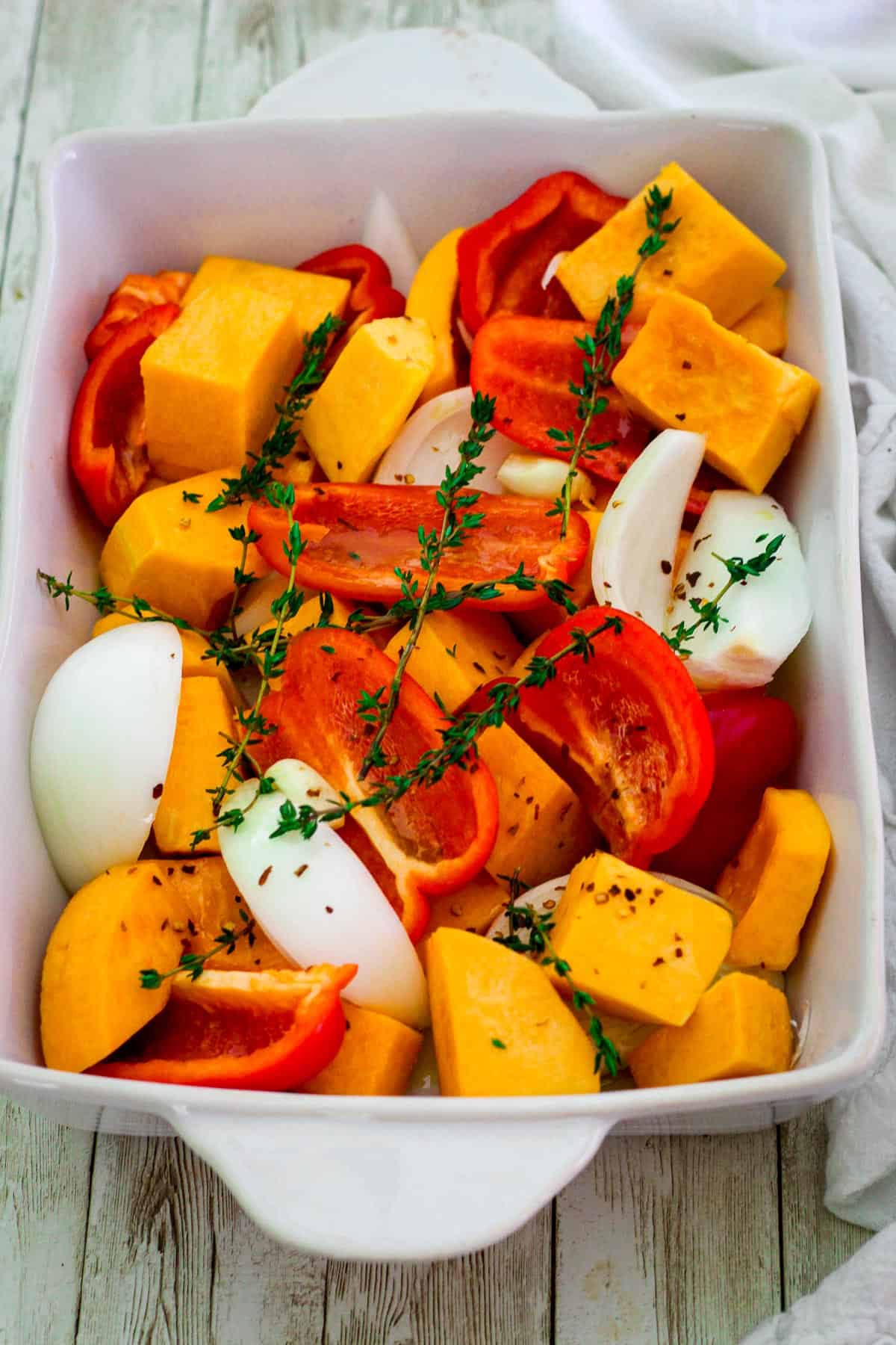 Fresh veggies on a baking tray, ready to roast. Visible are pieces of butternut squash, red pepper, onions and thyme. 