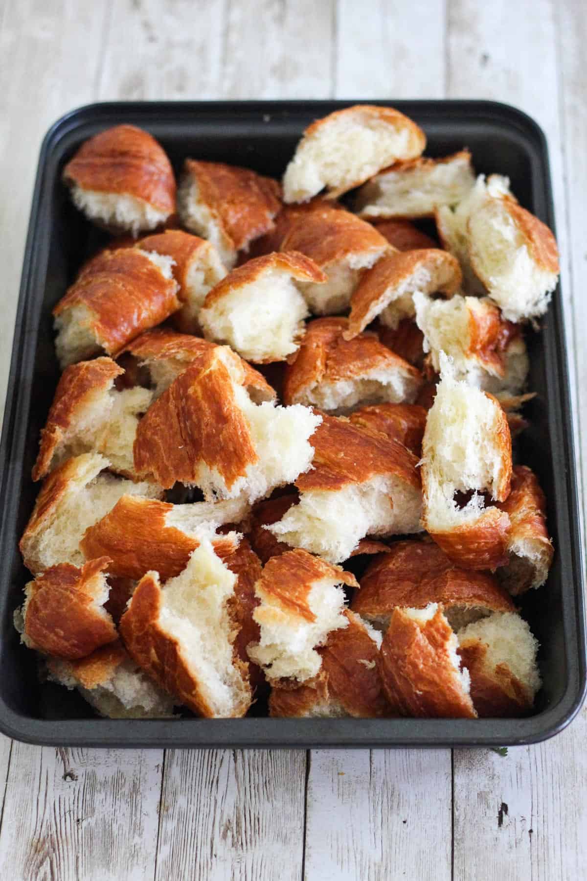 A baking dish with roughly chopped croissants in it. 