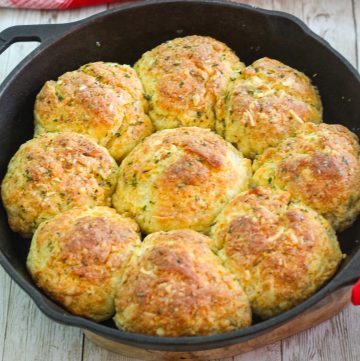 A cast iron skillet showing baked biscuits. There are 9 biscuits looking delicious next to each other on the skillet.