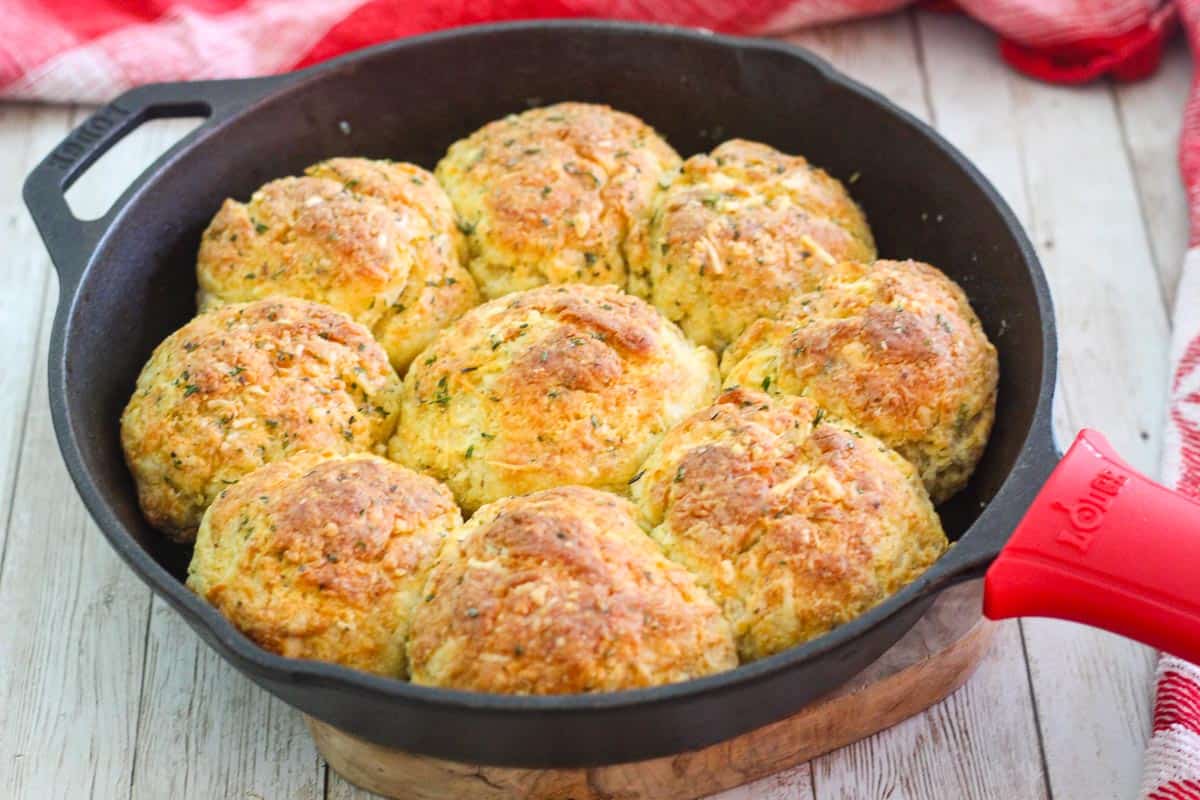 Baked three cheese biscuits in a cast iron skillet, skillet is placed on top of a wood piece to avoid burning the counter.