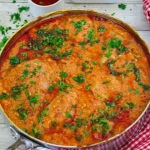 A deep skillet showing a chicken dish in a reddish sauce, garnished with fresh parsley on top.